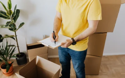 A man in a yellow shirt checks off a list while preparing for a move with cardboard boxes indoors