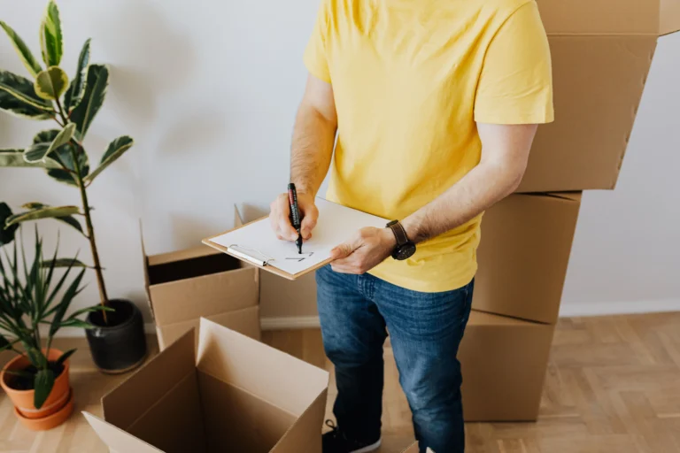 A man in a yellow shirt checks off a list while preparing for a move with cardboard boxes indoors