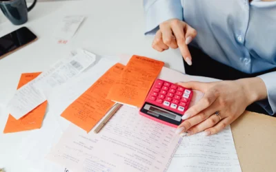 Hands using a pink calculator to manage expenses amidst various receipts and documents.