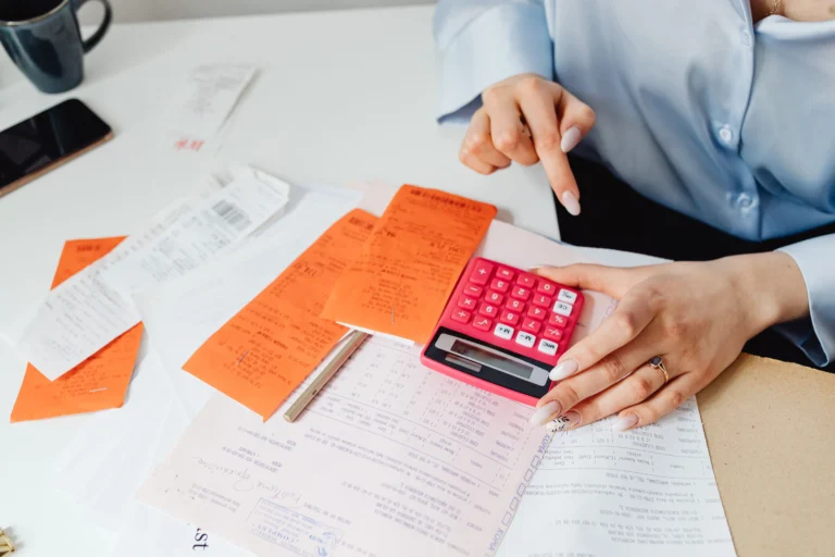 Hands using a pink calculator to manage expenses amidst various receipts and documents.