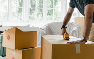 Man sealing cardboard boxes in a bright modern living room, preparing for a move.
