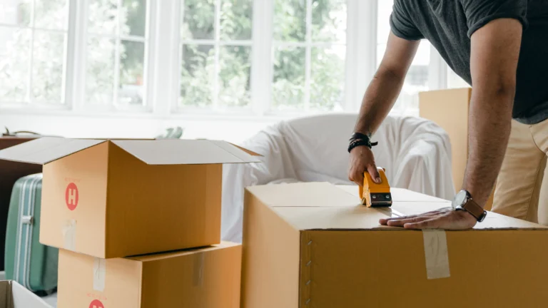 Man sealing cardboard boxes in a bright modern living room, preparing for a move.