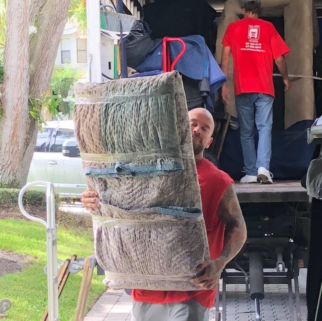 Red Box Moving crew unloading wrapped furniture in a South Florida neighborhood