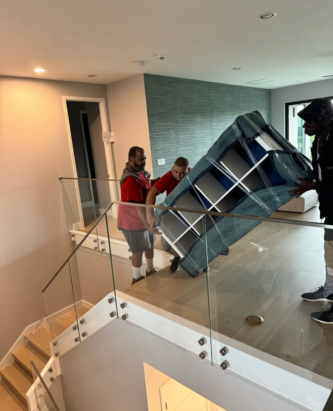 Red Box Moving crew carrying a wrapped sofa down a staircase in a Miami home