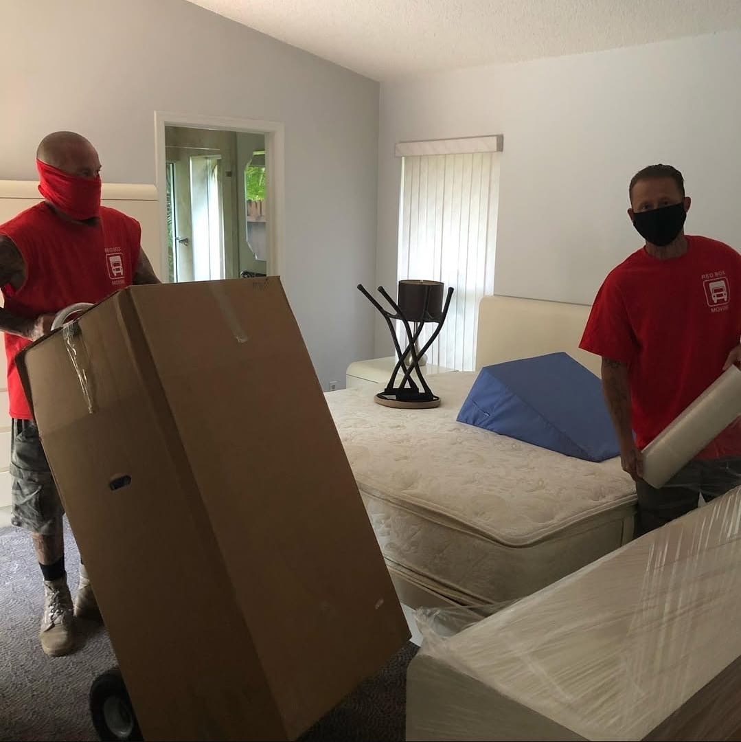 Red Box Moving crew packing and wrapping items in a Boynton Beach bedroom